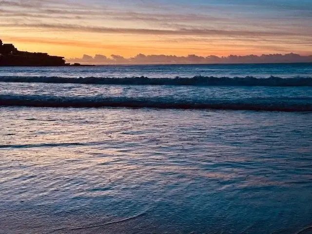 Calm ocean waves at sunset with colourful sky and horizon over the sea