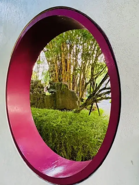 Garden view through circular wall opening with bamboo, greenery and outdoor landscape