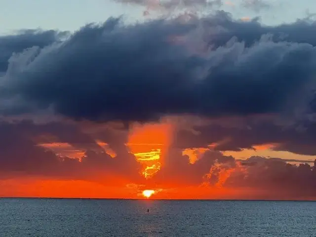 Vibrant ocean sunset with dramatic clouds and sun on the horizon over calm sea