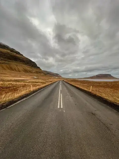 Long straight road through rugged landscape with mountains and dramatic cloudy sky