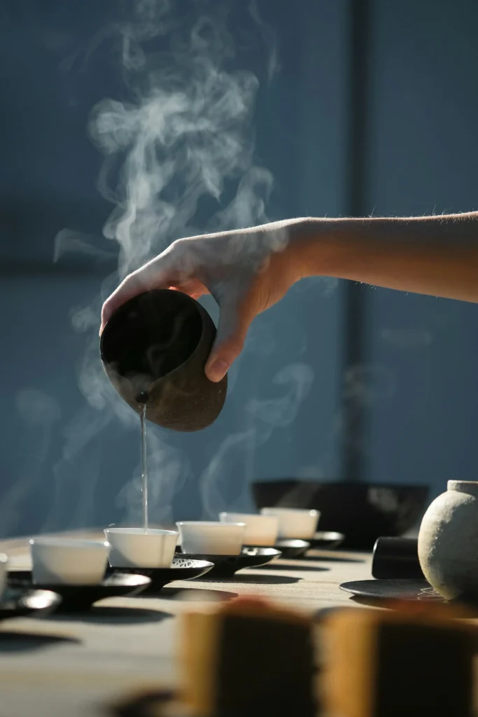 Hand pouring hot tea into cups with steam rising, creating calm and mindful atmosphere